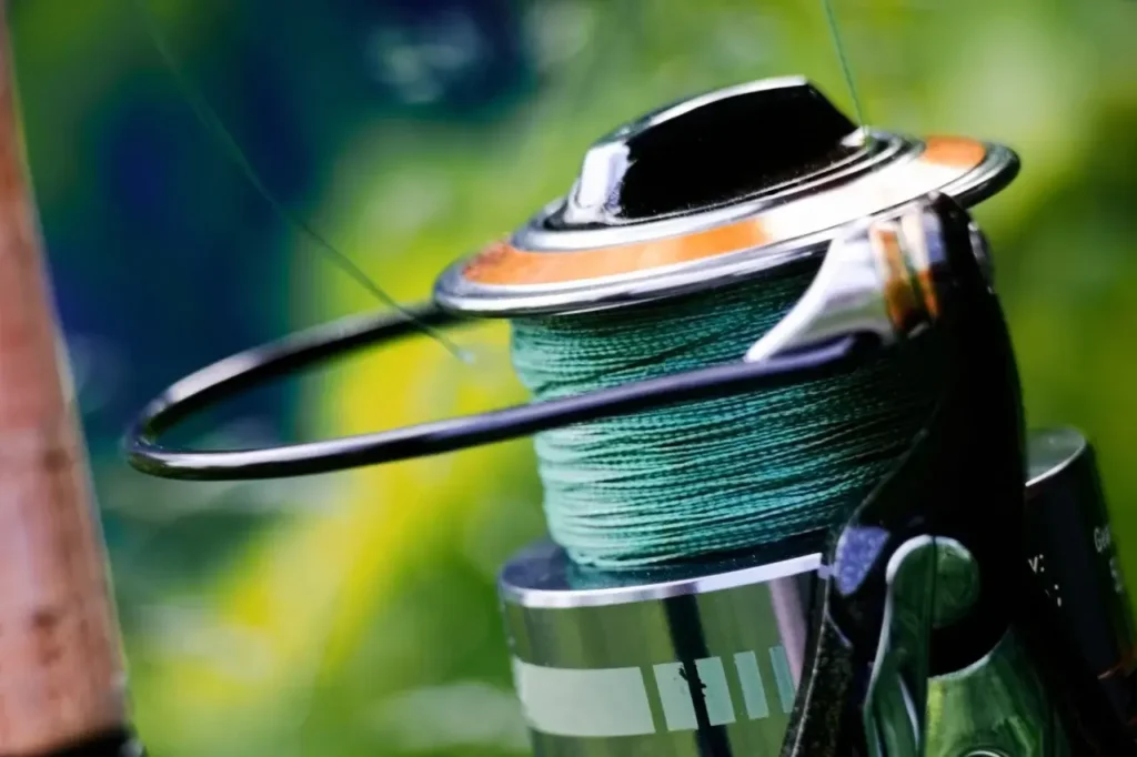 A close-up of a spinning reel with green fishing line is set against a blurred natural background.