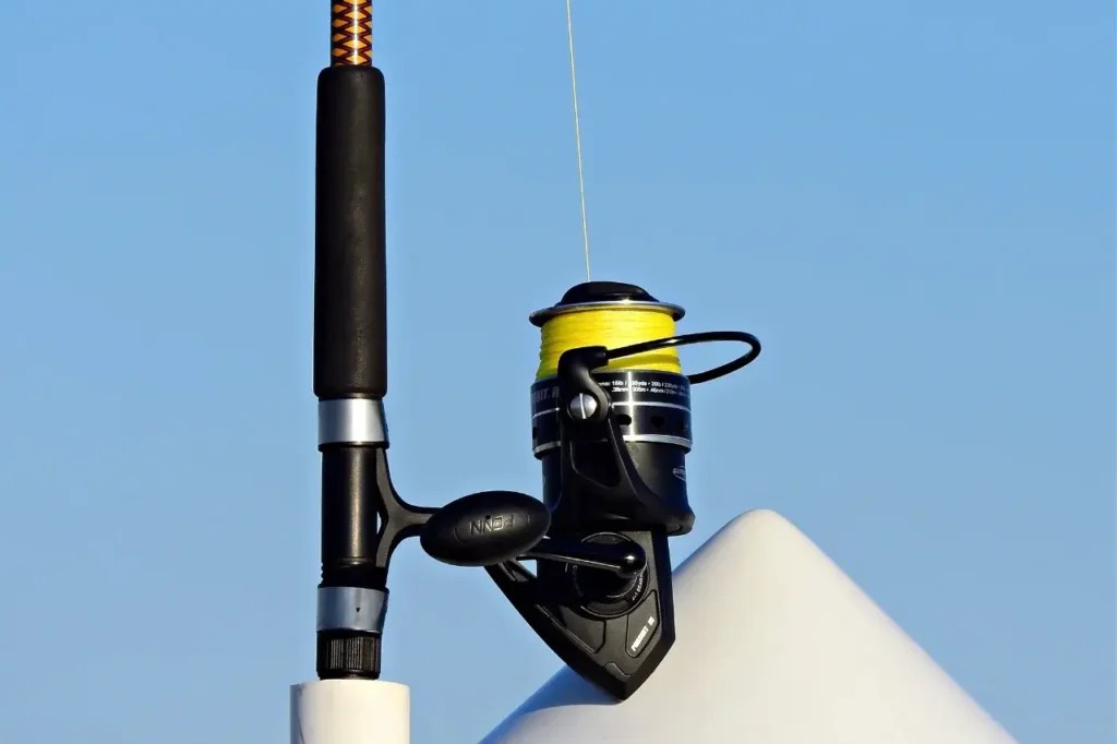 A spinning reel with bright yellow fishing line mounted on a fishing rod, set against a clear blue sky.