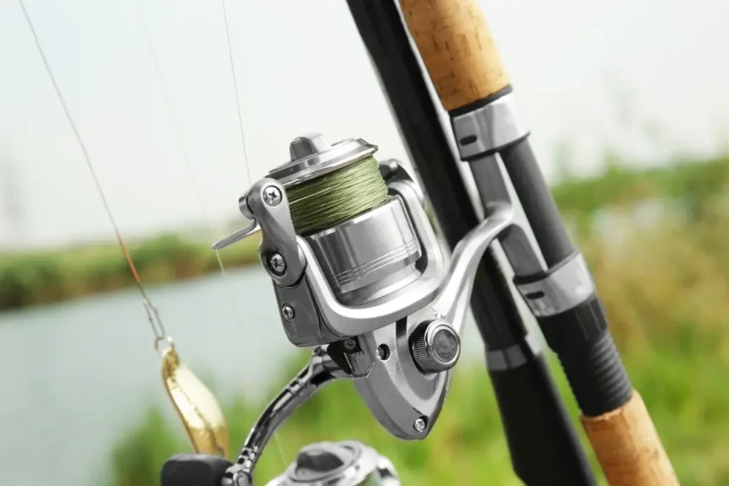 Close-up of a spinning reel on a fishing rod resting on a wooden dock near a peaceful lake at sunrise.