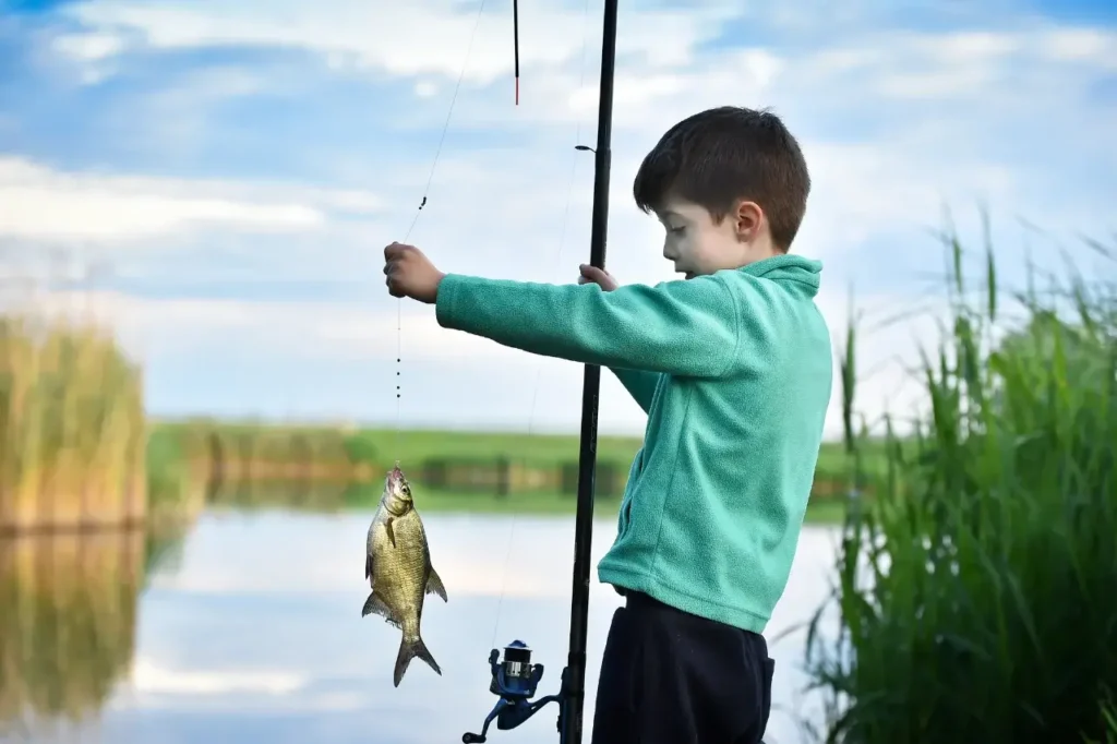A young boy holding up his freshly caught fish by the lake, excited about his fishing success.