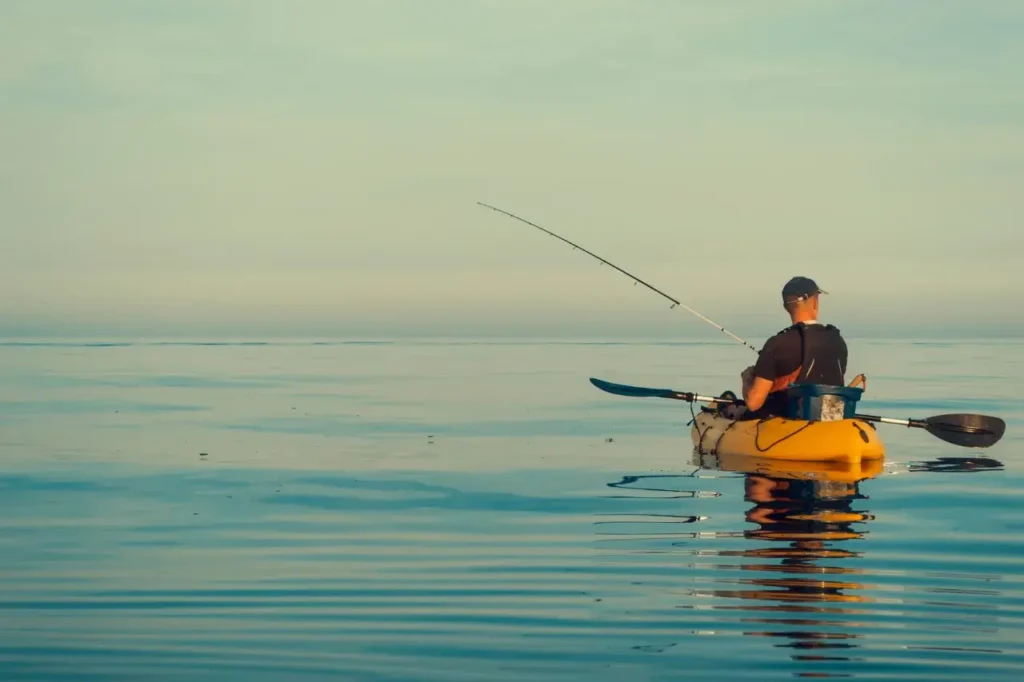 A solo angler fishing from a yellow kayak on calm waters, reflecting the morning sky, perfect for kayak fishing enthusiasts.