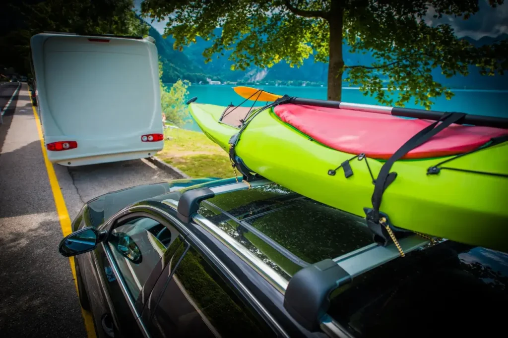 A securely strapped fishing kayak on top of a car, parked near a scenic lake, ready for an outdoor adventure.